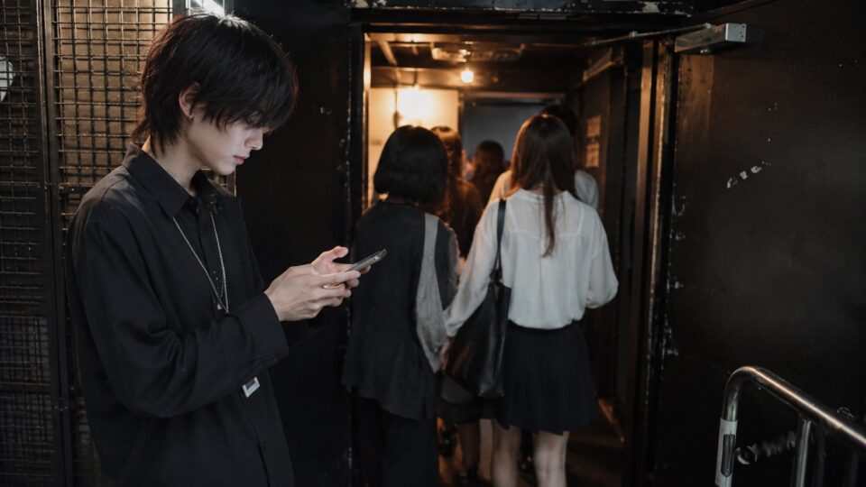 来場者が進むライブ会場の入口付近でスマートフォンを見る架空の成人男性
