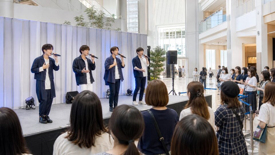 架空の商業施設の小さなステージで歌う男性アイドルと観客